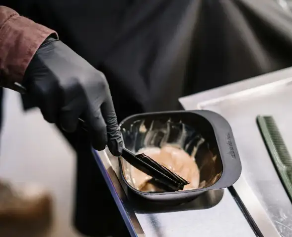A salon worker wearing a pair of black nitrile gloves is coloring a customer hair