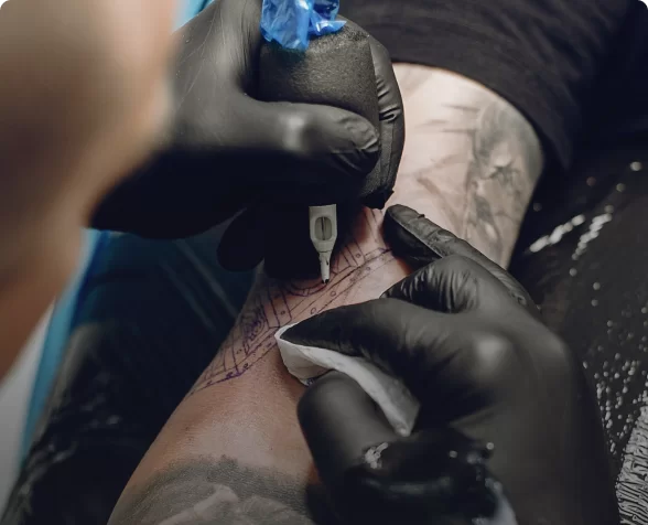 A tattoo artist wearing a pair of black nitrile gloves is tattooing a customer